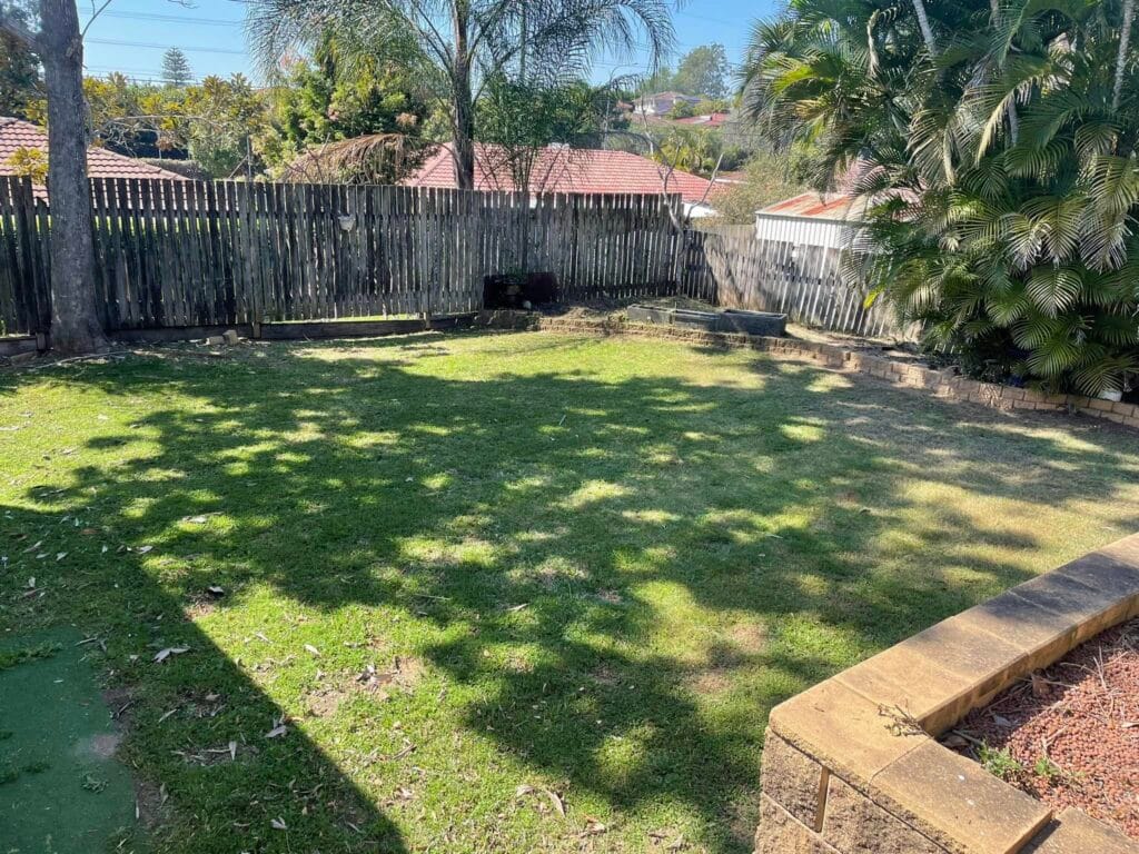Sunny backyard with grassy area and wooden fence.